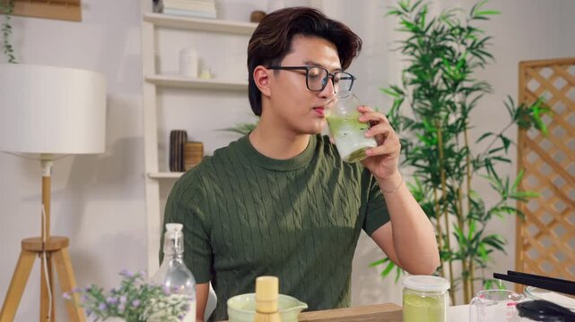 Portrait of Asian young man drinking matcha tea at table in cozy house. 