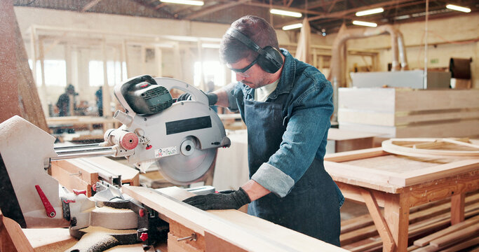 Man, carpenter and miter saw for wood at warehouse with manufacturing process at industrial plant. Person, tools and technician with equipment for cutting, material and safety goggles at factory