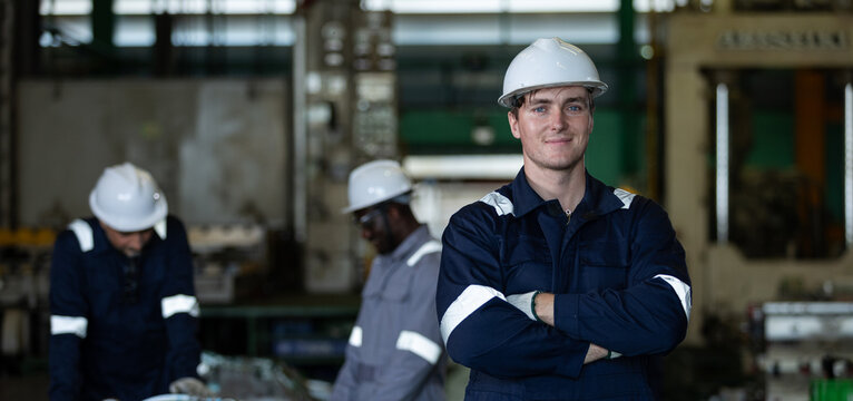 Industrial engineer standing with arms crossed in factory, confident professional worker leading manufacturing team, engineering leadership and workforce productivity in industrial operations.
