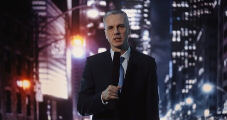 Fototapeta premium Serious Mature Man Journalist Delivering Live Report, Holding Microphone and Looking at Camera. Concept of Media Correspondence, Professional Portrait of Reporter Against Blurred City Night.