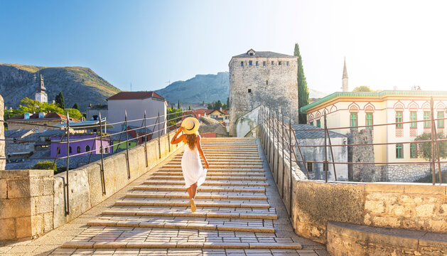 Woman in white dress walking on Stari Most bridge, sunset over old town Mostar, Bosnia and Herzegovina