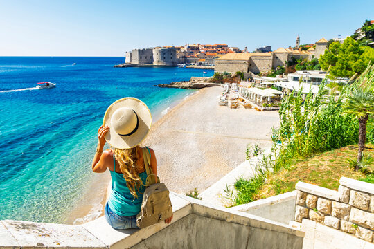 Woman tourist with straw hat looking at Banje beach and Dubrovnik old town, Adriatic Sea, Croatia