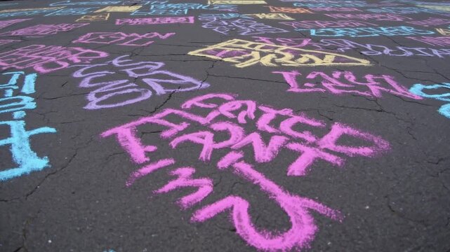 Colorful chalk graffiti covering courthouse steps, pastel messages and slogans scattered across pavement in front of neoclassical columns, activist markings, names and solidarity phrases, vibrant pink