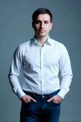 Fototapeta premium Portrait of young man standing with hands in pockets, looking at camera against plain background, with confidence and professionalism. Ideal for corporate, recruitment, leadership branding, vertical