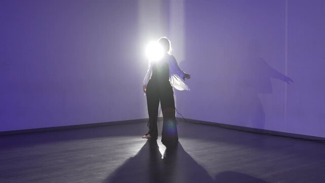 Dancer choreography silhouette practicing modern contemporary dance movements in dark studio with backlighting