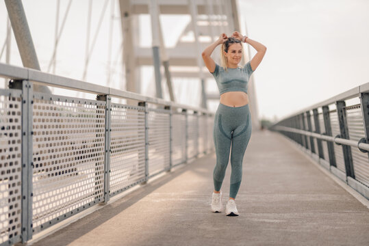 Sporty woman tying hair on modern bridge before workout
