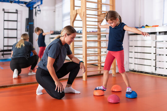 Trainer supervising a child performing corrective motoric balance training using sensory pods to improve neuromuscular coordination, stability and posture control  