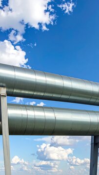 Two parallel metallic pipes against a vibrant blue sky dotted with puffy white clouds