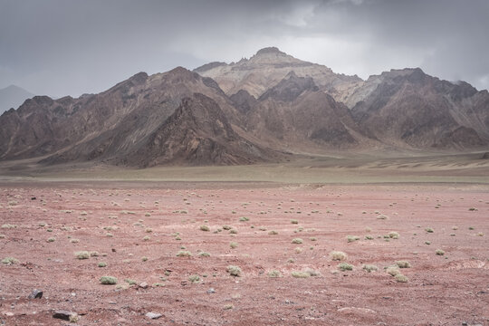 Desert terrain in the Tien Shan highlands of the Pamirs, a panoramic landscape of a desert plateau and rocky mountain range in cloudy weather in summer