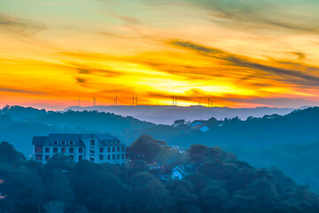 Obraz premium Breathtaking sunrise landscape with layers of misty hills and a glowing golden sky. Silhouettes of wind turbines stretch across the horizon, blending modern energy infrastructure