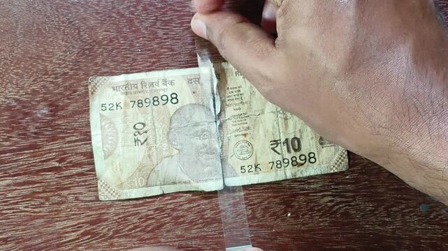 Indian broke adult person hand fixing or repairing torn india rupee currency note. Money devaluation, business loss, financial crisis, broken economy, no savings, rupees damage and poverty concept.