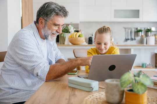 Grandfather and child learning together on a laptop in a kitchen