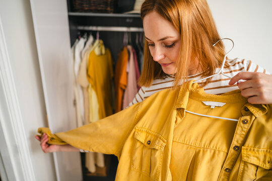 Woman choosing yellow shirt from overloaded wardrobe indoors
