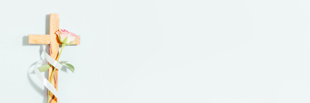 Wooden Christian cross with pale rose and ribbon placed on light background with wide copy space. Minimal horizontal faith banner for Easter greeting, church message, prayer post and worship design