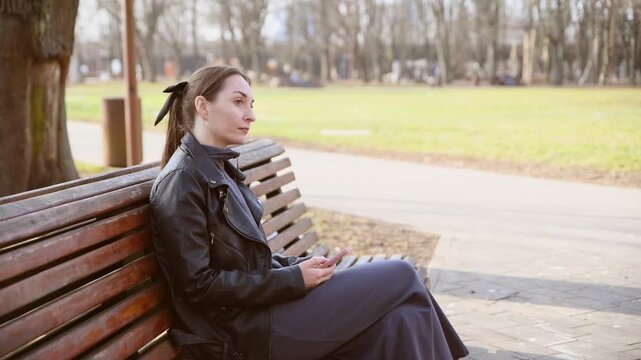 Young adult woman interacting with smartphone on outdoor park bench in soft daylight