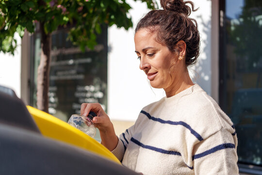 Woman recycling crumpled plastic bottle in yellow recycling bin outdoors