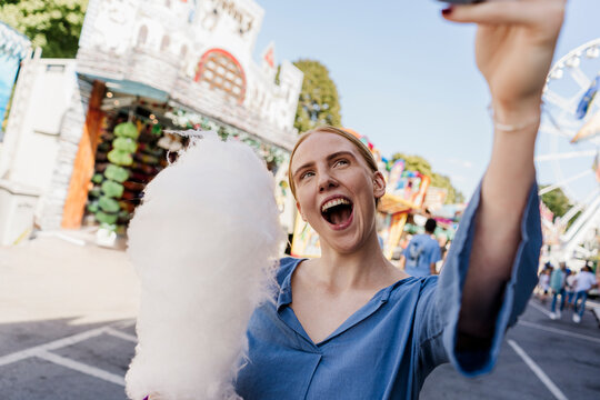 Happy woman taking selfie with cotton candy at colorful summer fair