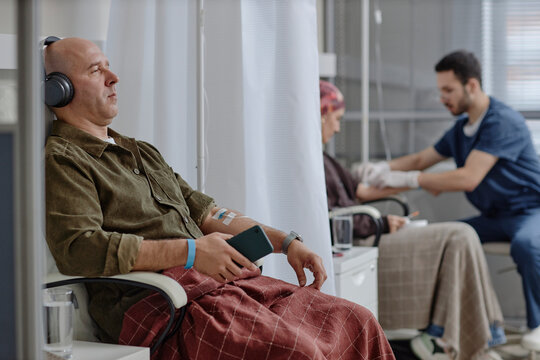 Patient receiving chemotherapy and relaxing with headphones at oncology clinic
