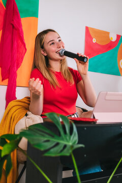 Smiling woman singing with microphone in home studio during online vocal lesson