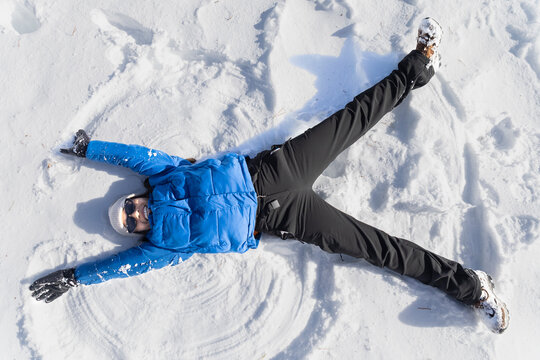 Woman in blue puffer jacket making snow angel in Pyrenees