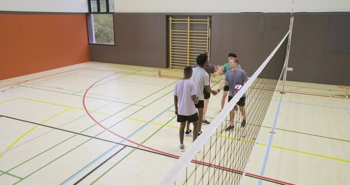 Five adult male players meeting at net in school gym, celebrating and adjusting purple volleyball