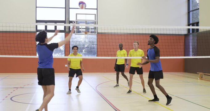 Diverse male players reacting to yellow serve, practicing rally with volleyball at school gym