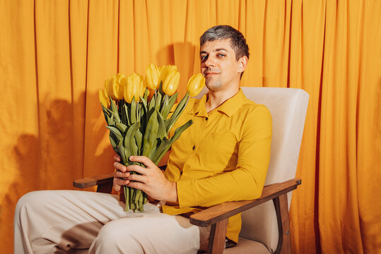 Portrait of man holding yellow tulip bouquet on chair indoors