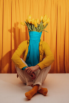 Creative man with tulips as head sitting in colorful indoor setting