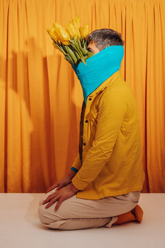 Kneeling man in yellow with tulips and blue scarf hiding face