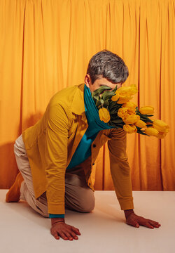 Man kneeling indoors with face hidden by yellow tulip bouquet