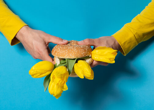 Hands holding creative spring burger with yellow tulip flowers