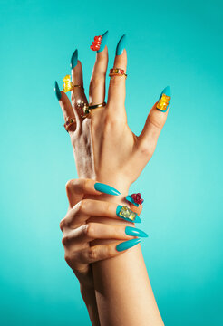 Hand with blue manicure and gummy bear nail art on turquoise background