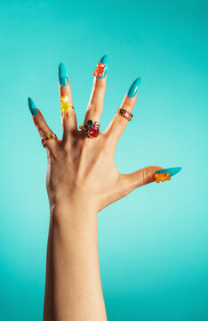 Hand with gummy bear nail art and rings on turquoise background