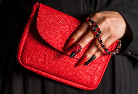 Hand with red manicure holding red textured bag and gummy bear jewelry