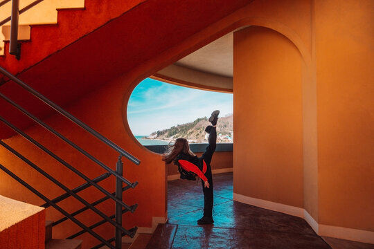 Teenage dancer kicking energetically by terracotta walls in daylight