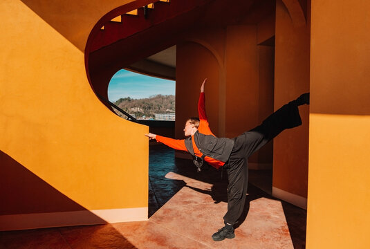 Young girl dancing energetically near terracotta architectural wall