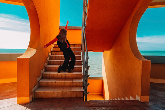 Teenager dancing energetically on stairs near terracotta walls and sea