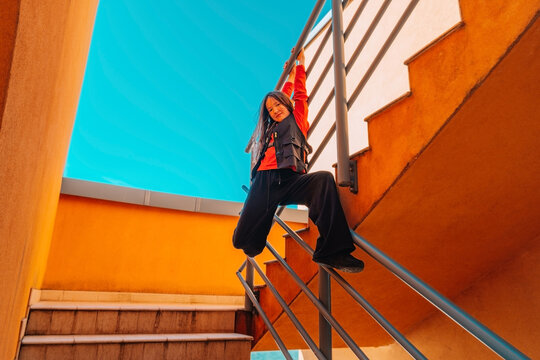 Teen girl energetically dancing on outdoor stairs with bright architecture