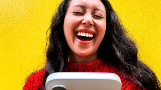 Laughing woman holding phone in front of yellow wall