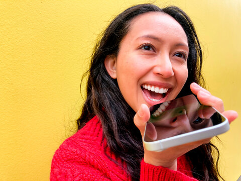 Smiling woman using voice assistant on smartphone outdoors