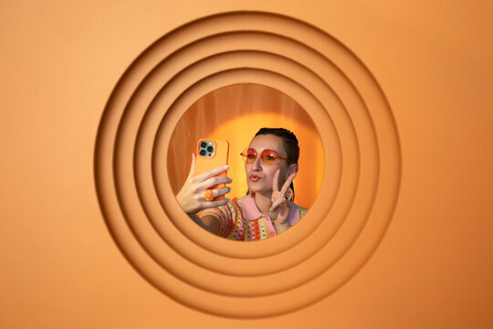 Trendy woman taking selfie with smartphone through orange circle
