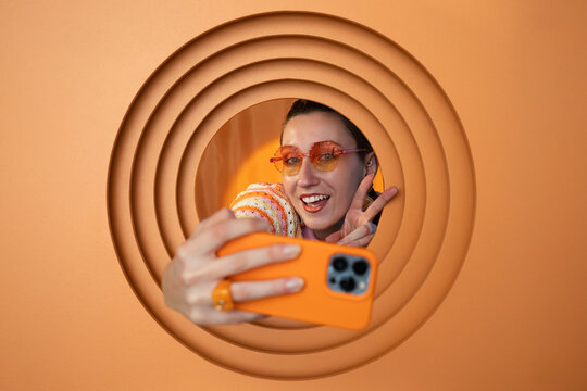 Happy person taking selfie with orange smartphone through circular backdrop