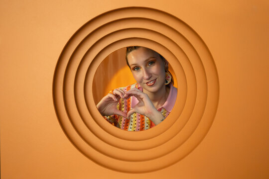 Smiling woman making heart gesture in orange setting