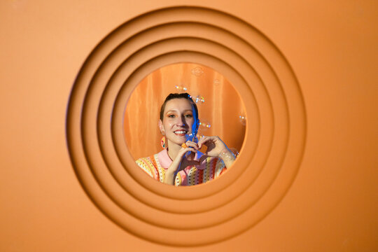 Smiling woman making a heart shape with hands surrounded by bubbles