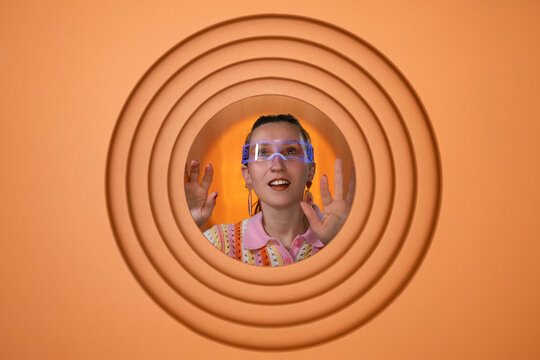 Woman wearing virtual reality goggles in front of orange circular background