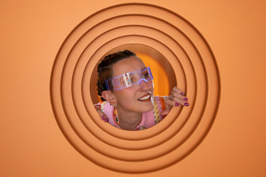Smiling woman in futuristic glasses looking through orange circular frame