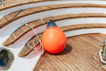 Orange inflatable marine fender on wooden steps of a luxury yacht deck near the water and mooring equipment © Dmitri