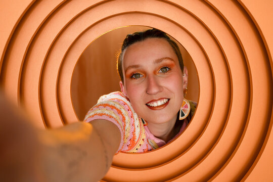 Smiling individual taking a selfie through circular orange frame