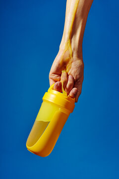 Hand gripping yellow shaker with orange protein drink dripping on blue