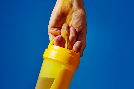 Yellow shaker bottle spilling thick orange fitness drink in hand